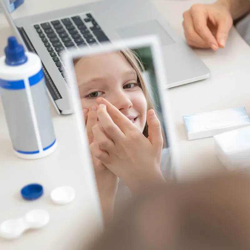 A young girl looking in a mirror as she puts in a contact lens